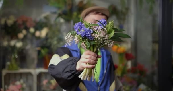 约会或浪漫的概念 满嘴牙签 头戴尖顶帽 身穿运动服的流氓男子站在花店里 伸出春天的花束 高质量的4K视频镜头 — 图库视频影像