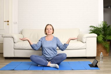 Evde, oturma odasında yoga yapan olgun bir kadın.