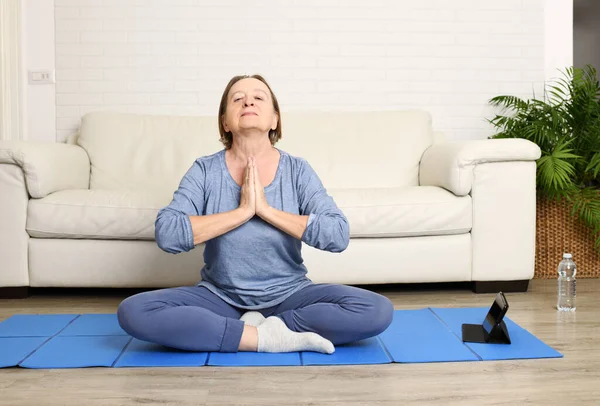 Evde, oturma odasında yoga yapan olgun bir kadın.