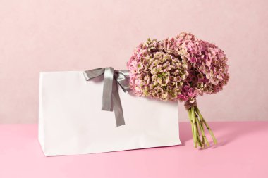 White shopping bag with beautiful bouquet on a pink background