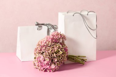 White shopping bags with beautiful bouquet on a pink background