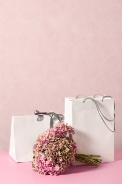 White shopping bags with beautiful bouquet on a pink background