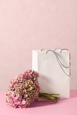White shopping bag with beautiful bouquet on a pink background