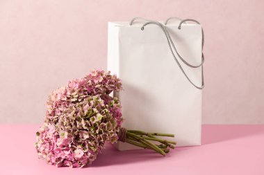 White shopping bag with beautiful bouquet on a pink background
