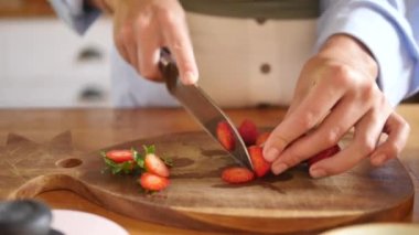 Kadın eli kesme tahtasının üzerinde çilek kesiyor.