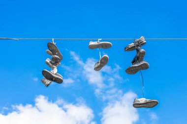 Mavi gökyüzünün arka planında kablolar üzerinde eski ayakkabılar.