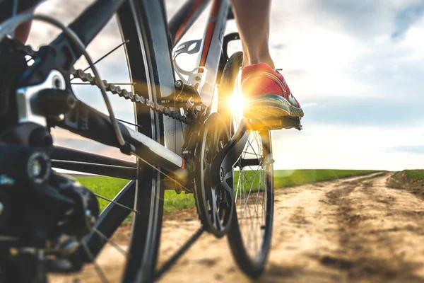 Foot on bike pedal at sunset. Close up rear view cyclist pedalling. Bicycle on the road. — Stock Photo, Image