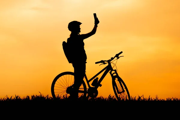 Silhouette einer Frau auf einem Fahrrad mit einem Telefon. Suche nach einem Telefonsignal. Verlorener Radfahrer. Smartphone-Navigation und Kartenanwendungen. — Stockfoto