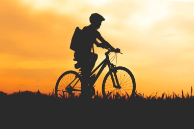 Gün batımında kasklı ve sırt çantalı bir bisikletçinin silüeti kırsala doğru yol alıyor..
