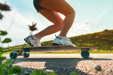 Güneşli bir günde asfalt yolda kaykay ya da uzun tahta üzerinde geniş açılı bacaklar. Dönen tekerleği kapat.