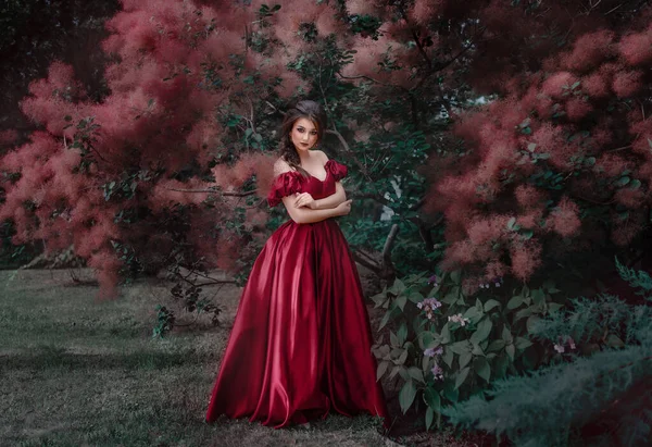 Mulher bonita em vestido vermelho andando no jardim cheio de rosas. — Fotografia de Stock