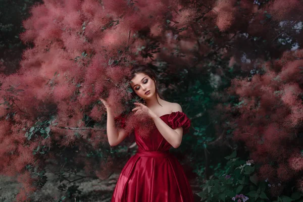 Mulher bonita em vestido vermelho andando no jardim cheio de rosas. — Fotografia de Stock