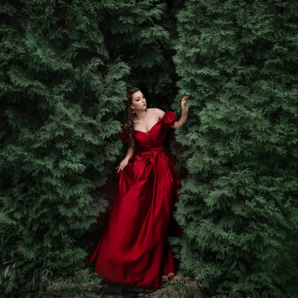 Schöne Frau in rotem Kleid spaziert durch den Garten voller Rosen. — Stockfoto