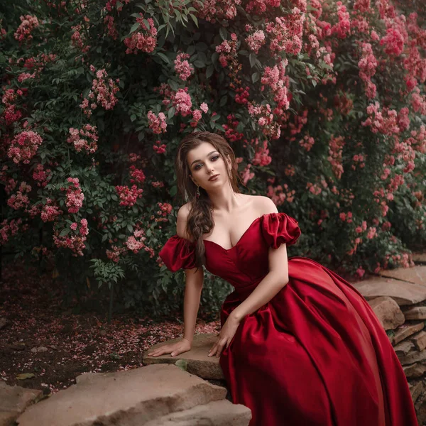 穿着红衣服的漂亮女人走在满是玫瑰的花园里. — 图库照片