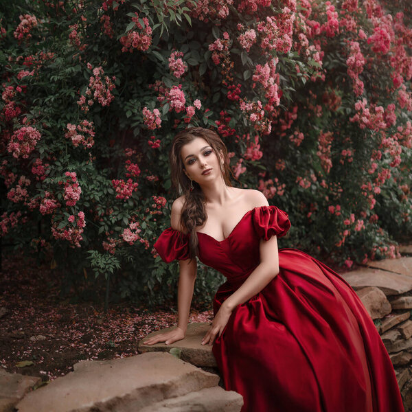 Beautiful woman in red dress walking in the garden full of roses.