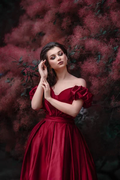 Vacker kvinna i röd klänning går i trädgården full av rosor. — Stockfoto