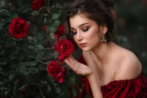 Belle femme en robe rouge marchant dans le jardin plein de roses. — Photo