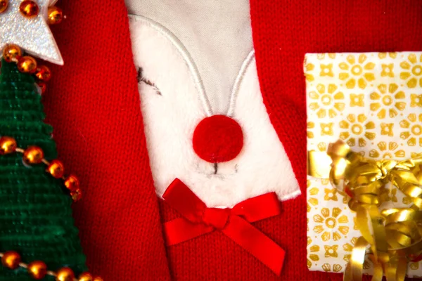Red New year sweater with funny deer face closeup. Small Christmas tree with silver star on top and present with golden ribbon on both sides. Winter party set. Postcard composition. Winter holidays — Stock Photo, Image