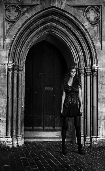 Young woman in a black dress against old stone gates outdoor shot — Stock Photo, Image