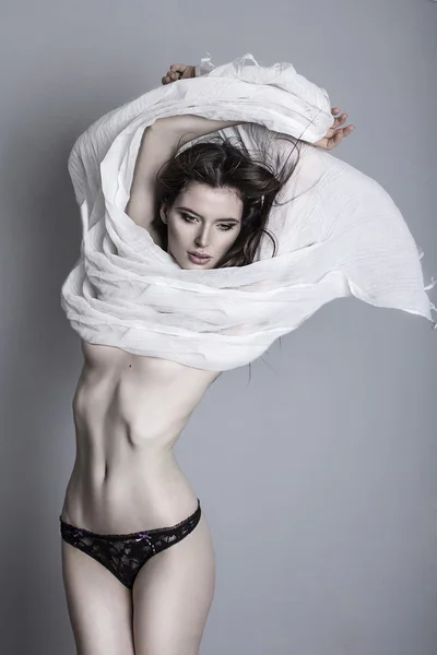 Jeune mannequin tenant un tissu blanc soufflé par le vent isolé en studio blanc tourné — Photo