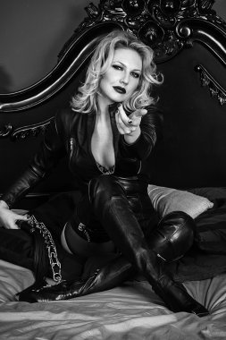 Genç sarışın seksi Bayan metres yatakta döşeme siyah deri kostüm giyen parlak kırmızı dudaklar