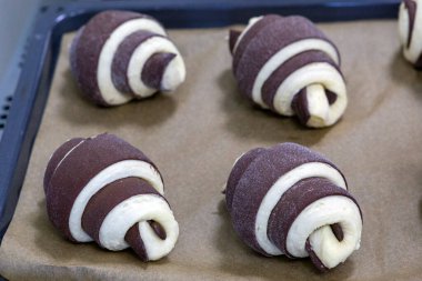 Çiğ hamurdan oluşan çikolatalı kruvasanlar fırına gönderilmeden önce fırın kağıdının üzerinde yatar. El yapımı hamur işi pişirme süreci