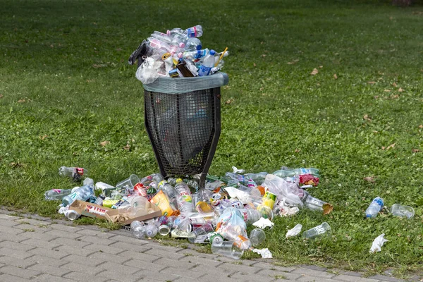 An overflowing trash can with rubbish lying around on the lawn