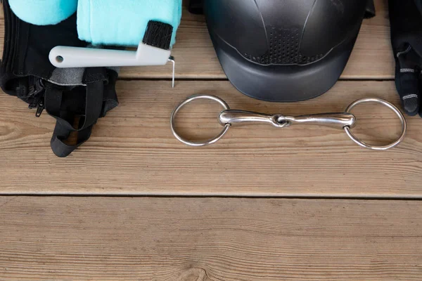 At bakımı için ekipman ve metin için kopyalama alanı: miğfer, kırbaç, eldivenler, dizgin, ahşap arka planda fırçalar