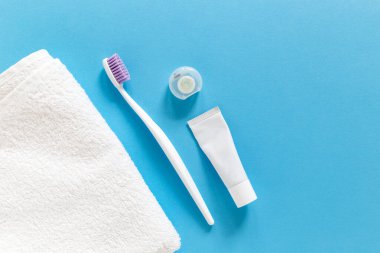 Flatlay of white towel, toothbrush, paste and dental floss on a blue background with copy space for your text. Morning routine and oral mouth and teeth hygiene concept