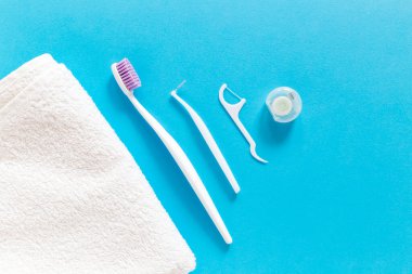 Flatlay of white towel, toothbrush, dental floss and other toiletries on a blue background. Morning routine and oral mouth and teeth hygiene concept