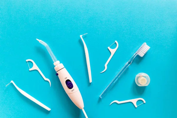 Flatlay of toothbrush, dental floss, irrigator and other toiletries on a blue background. Modern morning routine and oral mouth and teeth hygiene concept