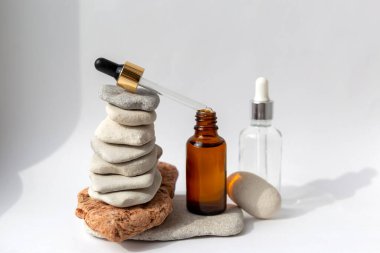 Beyaz arka planda pipeti olan şeffaf bir şişesi olan çok renkli taşlardan kule. Kozmetik ürünlü doğal podyum