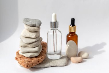 Beyaz arka planda pipeti olan şeffaf bir şişesi olan çok renkli taşlardan kule. Kozmetik ürünlü doğal podyum
