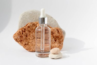 Beyaz arka planda pipeti olan saydam bir şişesi olan çok renkli taşlar. Kozmetik ürünlü doğal podyum