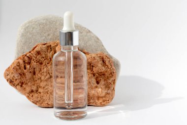 Beyaz arka planda pipeti olan saydam bir şişesi olan çok renkli taşlar. Kozmetik ürünlü doğal podyum