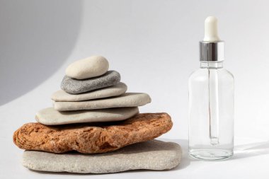 Beyaz arka planda pipeti olan şeffaf bir şişesi olan çok renkli taşlardan kule. Kozmetik ürünlü doğal podyum