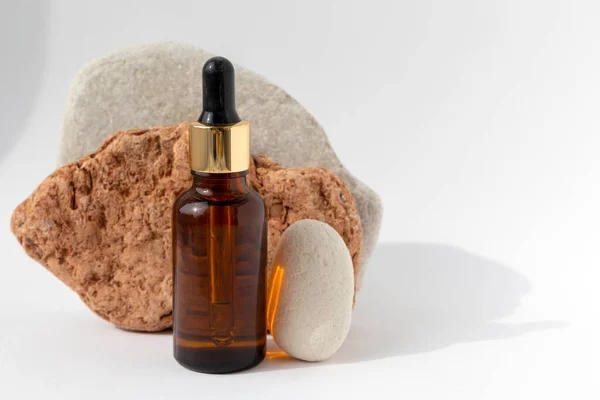 Beyaz arka planda pipeti olan kahverengi yağ şişesi olan çok renkli taşlardan kule. Kozmetik ürünlü doğal podyum