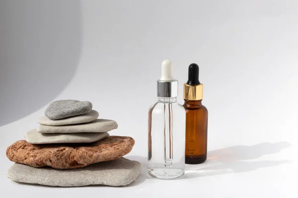 Beyaz arka planda pipeti olan şeffaf bir şişesi olan çok renkli taşlardan kule. Kozmetik ürünlü doğal podyum