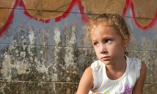 Sad little girl on background the wall — Stock Photo, Image