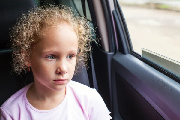 Sad little girl sitting in the car near the window — Stock Photo, Image