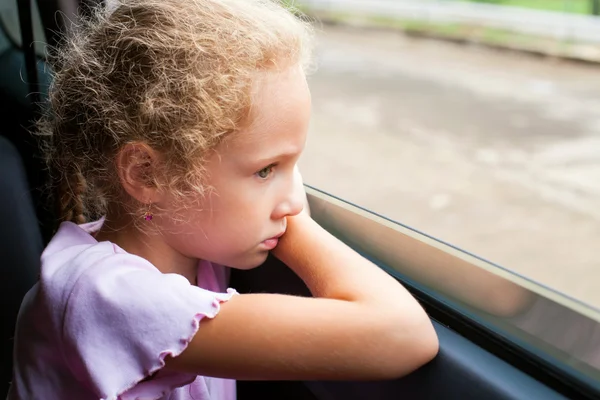 Ledsen liten flicka sitter i bilen nära fönstret — Stockfoto