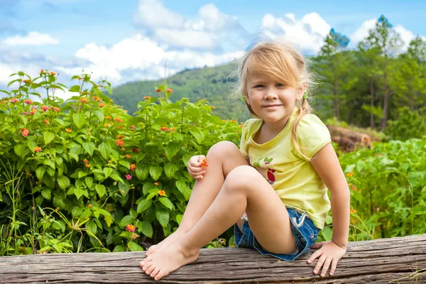 Criança feliz senta-se em um tronco no fundo das montanhas — Fotografia de Stock