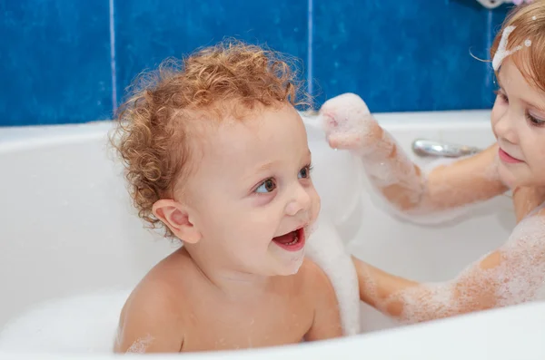 Little brother and sister taking a relaxing bath with foam.