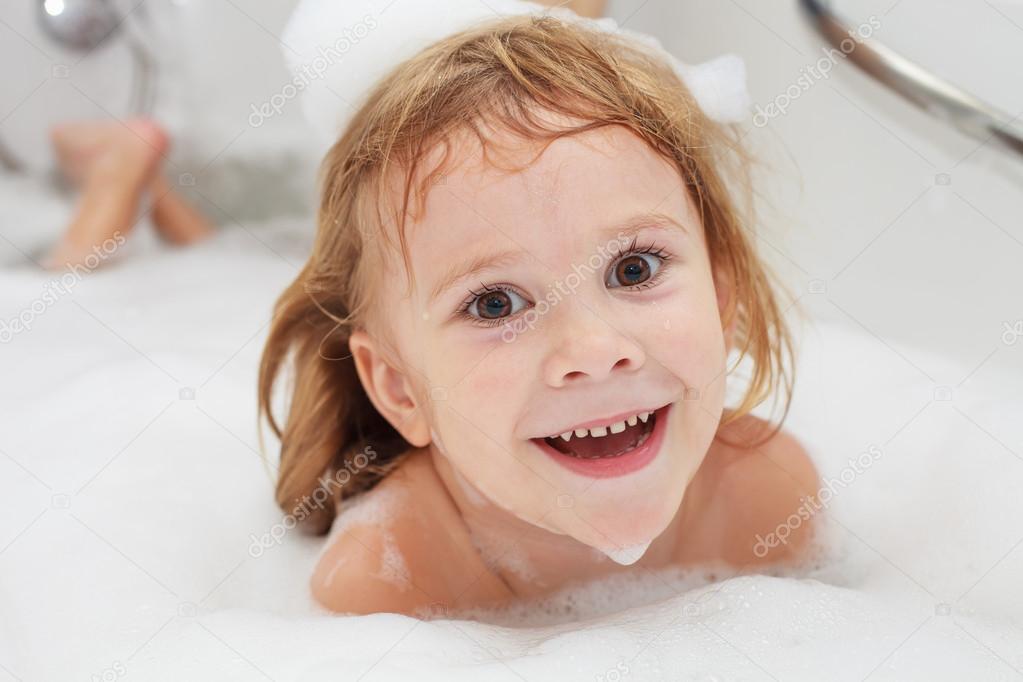 Cute four year old girl taking a relaxing bath with foam.