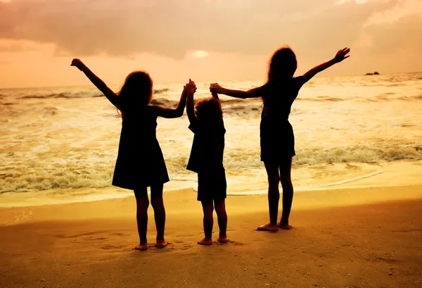 Drei Kinder Silhouetten stehen am Strand bei Sonnenuntergang — Stockfoto