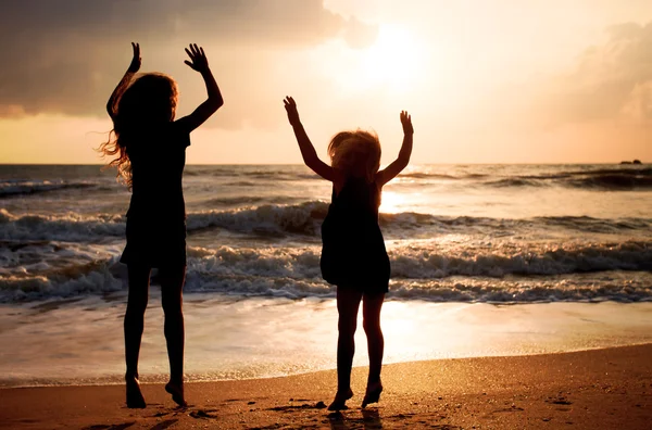 Two happy girls jumping on the beach on the dawn time — Stock Photo, Image