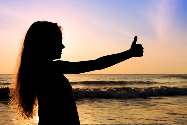 Happy girl shows gesture cool on beach at dawn — Stock Photo, Image