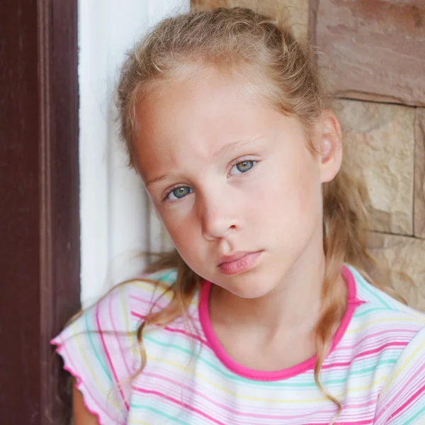 Ledsen liten flicka sitter nära en dörr på bakgrund av en bric — Stockfoto