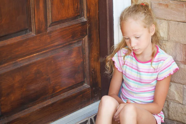 Smutný holčička sedí u dveří na pozadí bric — Stock fotografie