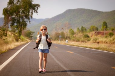 Sırt çantalı küçük kız yolda yürüyor.